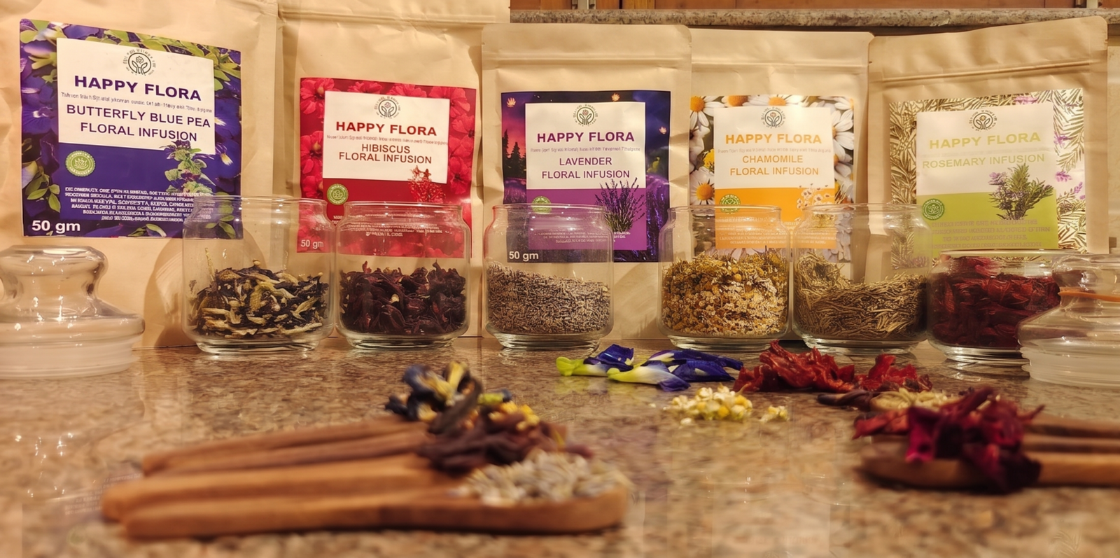 Happy Flora's full range of premium loose floral infusions, showing five stand-up kraft pouches in a row with small wooden spoons in front displaying uncrushed botanical petals like Lavender, Hibiscus, and Rhodendron.